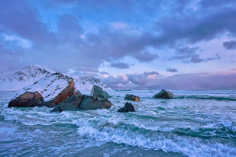 Waves of Norwegian sea on rocky coast in fjord on sunset with sun. Skagsanden beach, Lofoten
