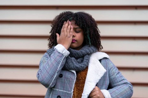 Black ethnic woman making a stop racism gesture on a gray wall, covering her eyes