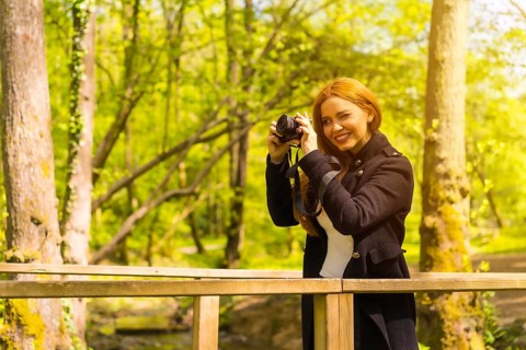 Woman photographer with a black jacket enjoying in an autumn park, taking pictures at sunset on a