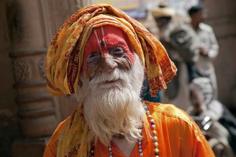 Old Hare Krishna follower dressed in orange dress in front of temple in Govardhan, India, Asia