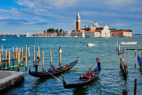 VENICE, ITALY, JUNE 27, 2018: Gondolier with tourists in gondola in lagoon of Venice by Saint Mark