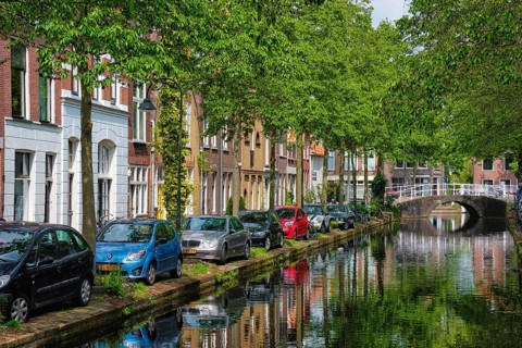 Delft, Netherlands, May 12, 2017: Cars and bicycles parked on canal embankment in street of Delft