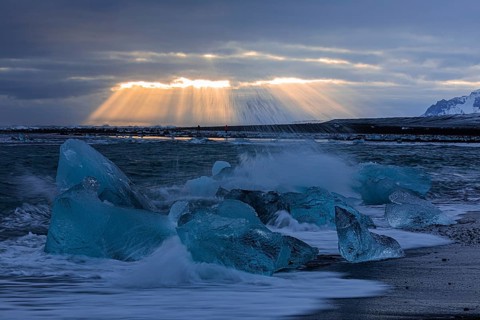 Waves breaking on icebergs on the black beach of Breidamerkursandur, sunset, near Jökullsarlon,