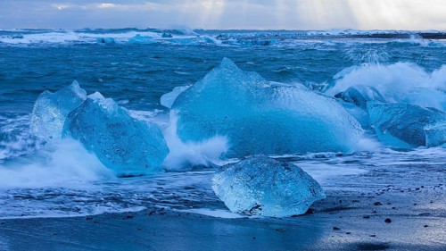 Waves breaking on icebergs on the black beach of Breidamerkursandur, near Jökullsarlon, Sudurland,