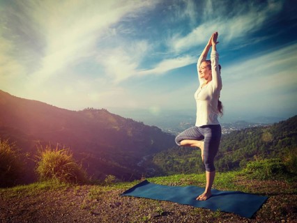 Yoga practice outdoors, woman practices balance yoga asana Vrikshasana tree pose in Himalayas