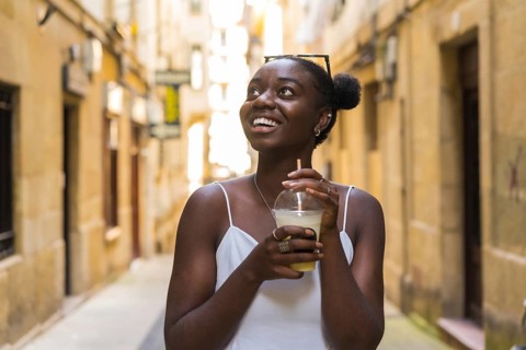 African woman looking up with amazed expression while drinking a take away milkshake visiting a
