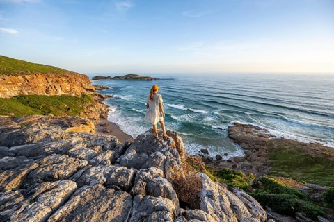 Young woman standing on a rock above the sea in the evening light, beach at The Gap, Robberg