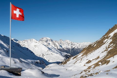 Swiss flag in front of mountain landscape in winter, mountain panorama with the peaks of the