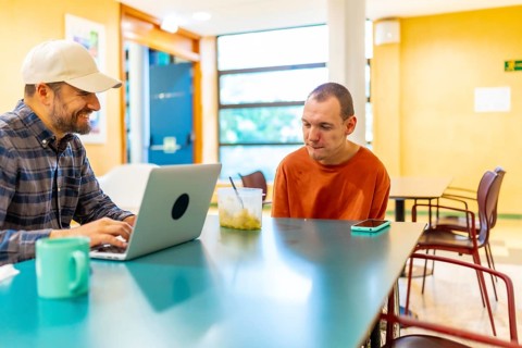 Cauasian adult man with disability and colleague working in the cafeteria of coworking
