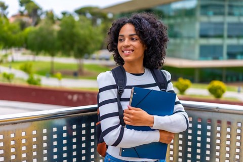 Latin female student smiling standing outside the campus of the university holding folder and