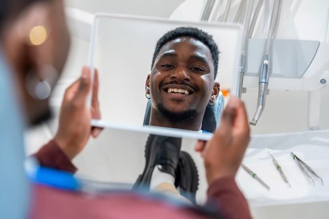 Happy patient looking at his whiter teeth in the mirror at the dental clinic after a whitening