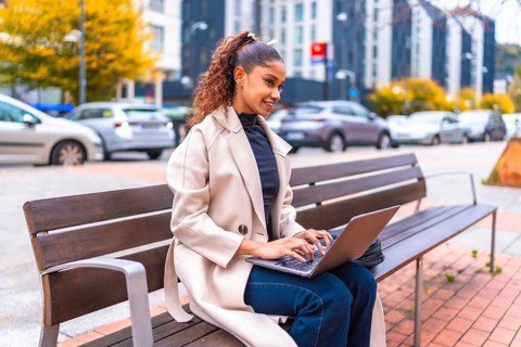 African american elegant businesswoman sitting on a bench using laptop in the city in autumn