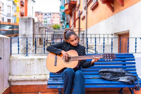 African american beauty woman playing acoustic guitar sitting in a blue bench in the city
