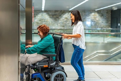 Side view of a chinese female caregiver pushing wheelchair of a caucasiana adult disabled woman