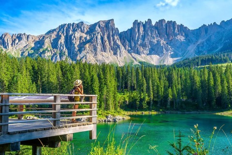 Female tourist admiring the stunning landscape of lake carezza with the latemar massif in the