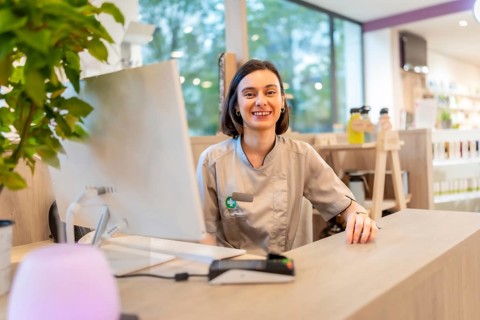 Cheerful young caucasian saleswoman smiling at camera while working on the counter of a pharmacy