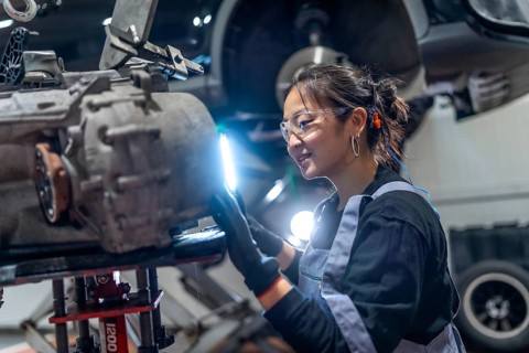 Skilled female mechanic wearing safety glasses and earplugs, meticulously inspecting a gearbox in a