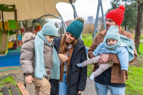Happy family with two children having fun together at the playground during a cold winter day