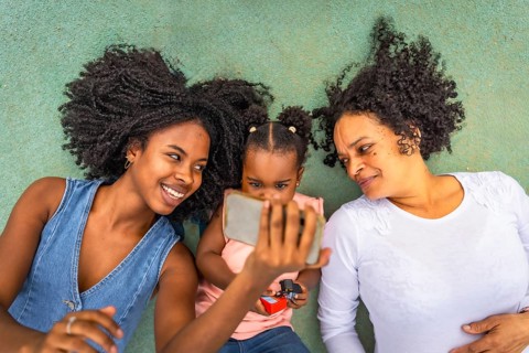 Top view of three african multi-generation woman watching the screen of the mobile lying down in a