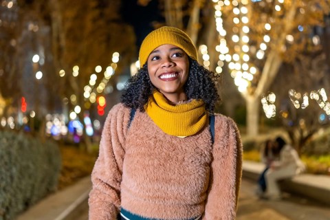 Portrait of a young black woman wearing winter clothes, smiling in a christmas decorated city at