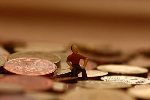 Miniature man sitting among euro coins, North Rhine-Westphalia, Germany, Europe