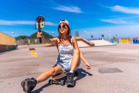 Smiling chinese female vlogger filming at skateboard park in summer