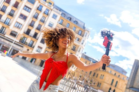 Dynamic photo of a happy latin young female vlogger streaming online using phone in the city