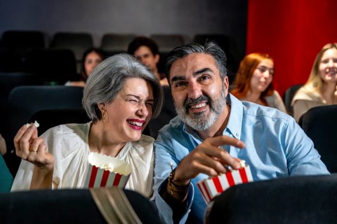Mature couple having fun watching a comedy film at the movie theater, sharing popcorn and laughing