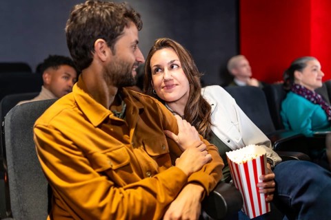 Couple enjoying a cozy movie night, sharing popcorn and affection while surrounded by a lively