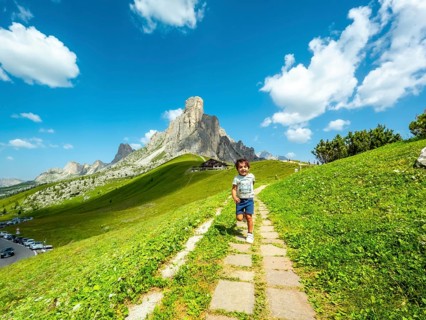 Happy child running on a path at giau pass in the italian dolomites with a mountain peak and blue