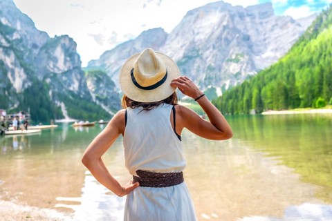 Woman wearing straw hat, enjoying the amazing view of lake braies in the dolomites mountains during