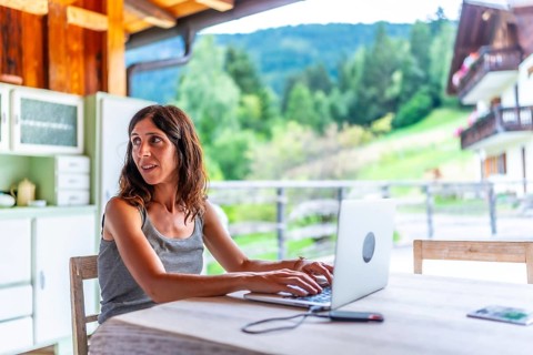 Freelancer woman working remotely on vacation with a laptop in a mountain chalet, enjoying the view