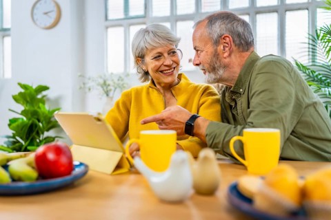 Mature couple exploring the net using digital tablet together at home while having breakfast