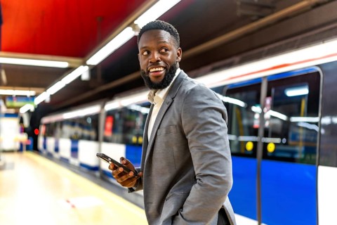 Young black businessman waiting for subway train while using his smartphone and looking away
