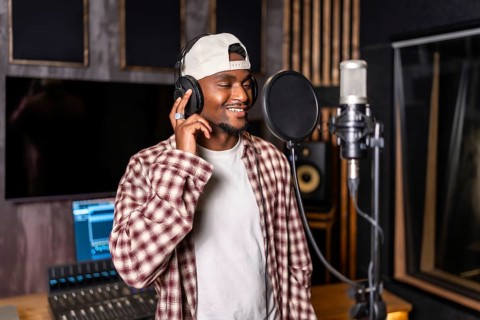 Young happy african american male singer wearing headphones and recording a song in professional
