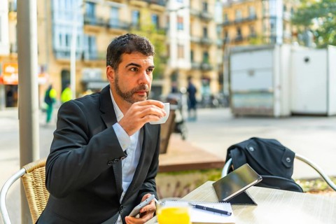 Businessman enjoying morning coffee while working with smartphone and digital tablet in an outdoor