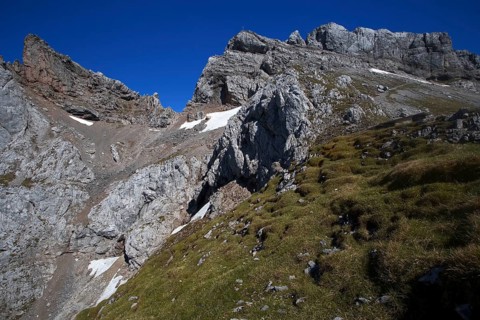 Steep mountain face with scattered snow fields and green grassy areas under a clear sky, Karwendel,