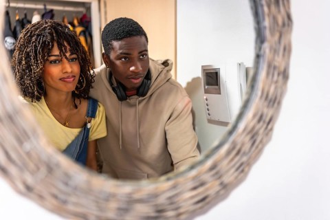Young multiethnic couple looking at intercom screen reflected in a mirror in the entrance hall of