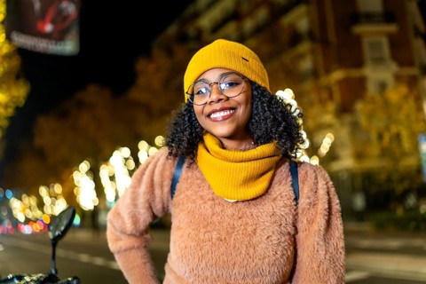 Portrait of a young woman wearing winter clothes and smiling in a city street decorated with