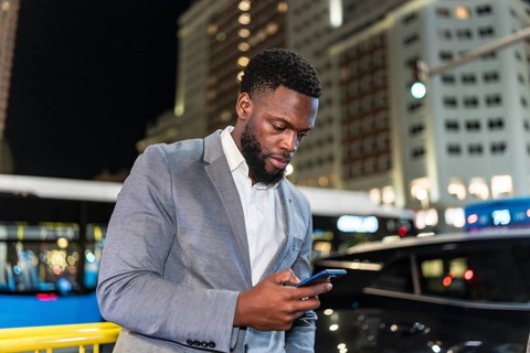 Young businessman using smartphone on a city street at night, with office buildings and traffic in
