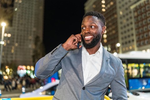 Young businessman smiling and chatting on a smartphone in a vibrant urban city at night, surrounded