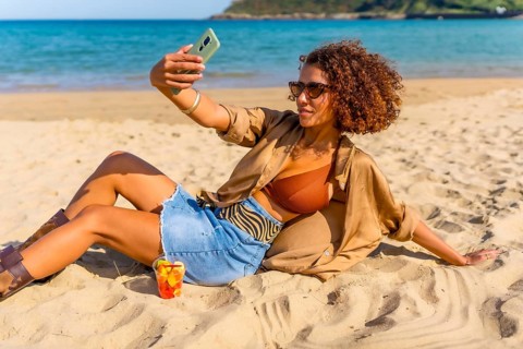 Confident woman in summer clothes taking selfie leaning on sandy beach
