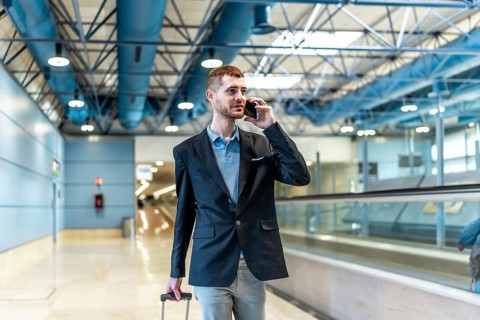 Businessman pulling suitcase and making phone call while walking through airport terminal