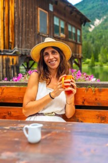 Woman wearing a straw hat enjoying a hot beverage in a mountain chalet by the lake in the italian