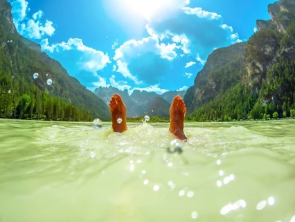 Feet of a tourist floating in the turquoise water of lago di landro, surrounded by the breathtaking