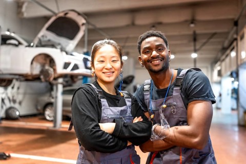 Two smiling mechanics with arms crossed, showcasing confidence and professionalism in a busy car