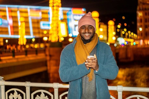 Smiling african man holding a warm cup of coffee in the city in a Christmas season night