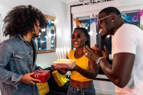 Friends surprising latin man with birthday cake and present celebrating a party at home at night