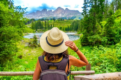Female tourist with backpack and straw hat admiring the beautiful landscape of lake carezza and