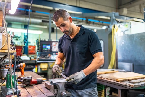 Caucasian adult male manual worker working in metal factory using drill and manual tools